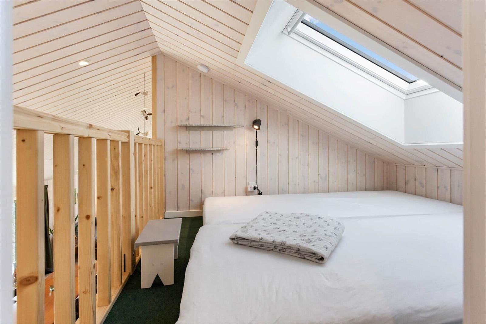 Schlafzimmer mit Dachfenster, Holzwand und Bett mit Decke.