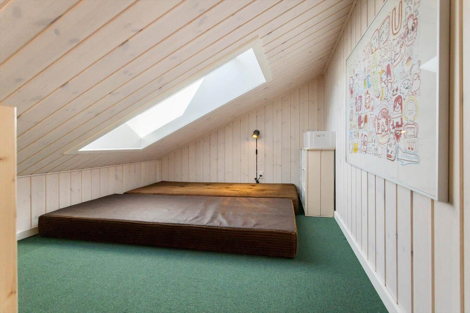 Zimmer mit Dachschrägen, Schlafcouch und großem Fenster. Wand mit Zeichnungen.