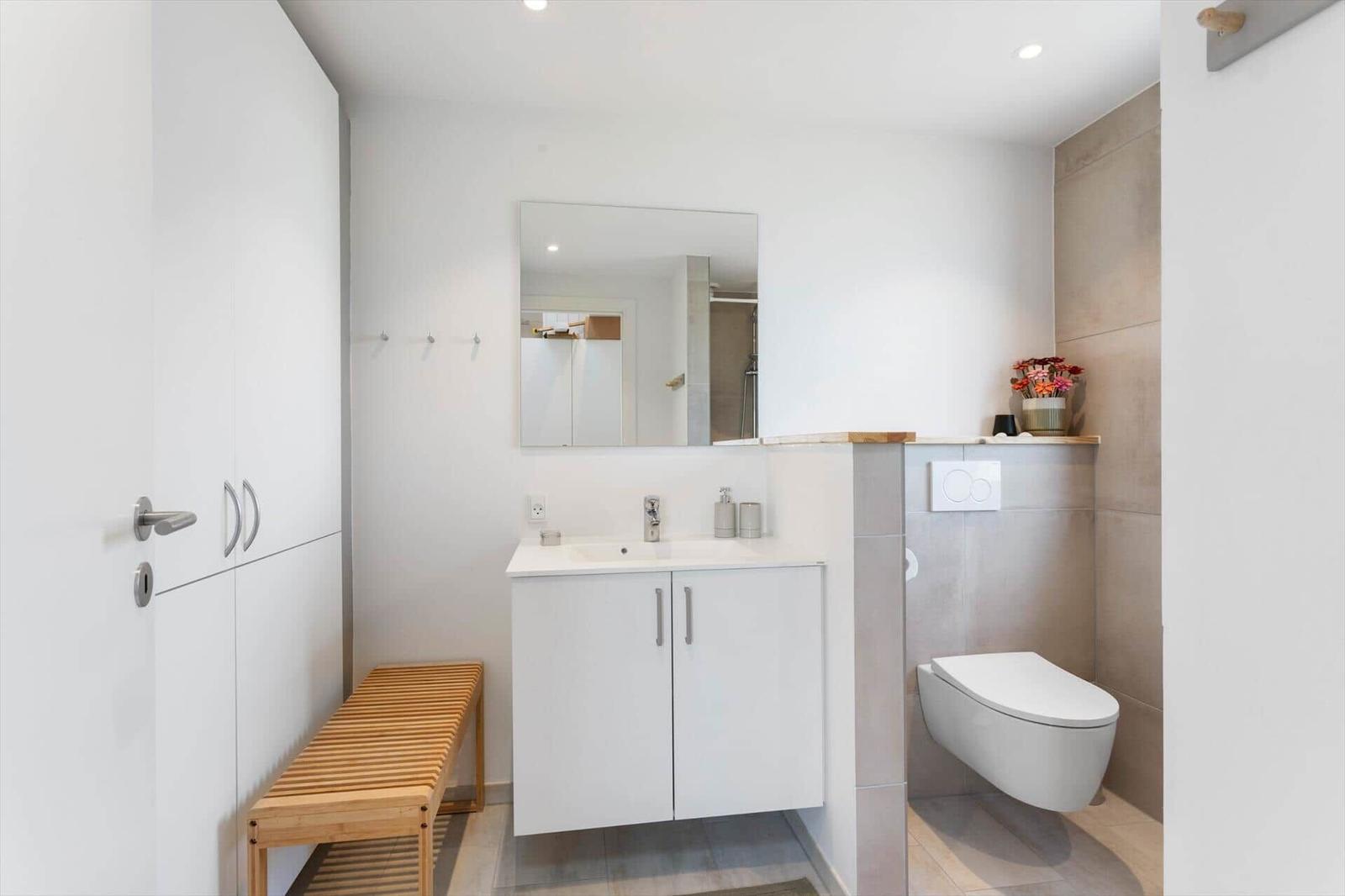 Badezimmer mit Waschbecken, Spiegel, Toilette und Holzbank.