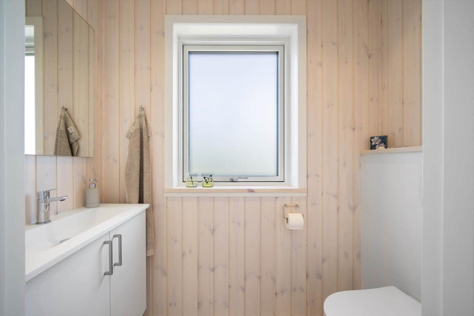 Badezimmer mit Holzwand, Waschbecken, Toilette und Fenster