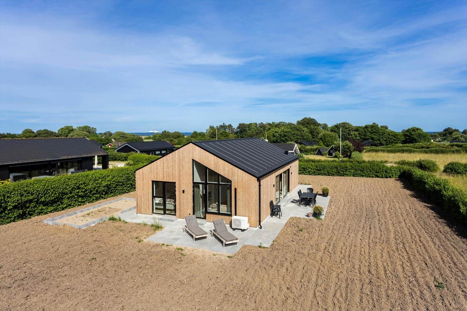 Moderne Holzhütte mit Terrasse, Liegen und Blick auf die Landschaft.