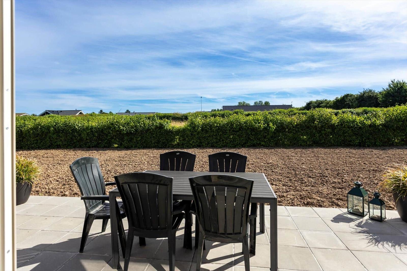 Terrasse mit Tisch und Stühlen, Blick auf grüne Hecke und Himmel.