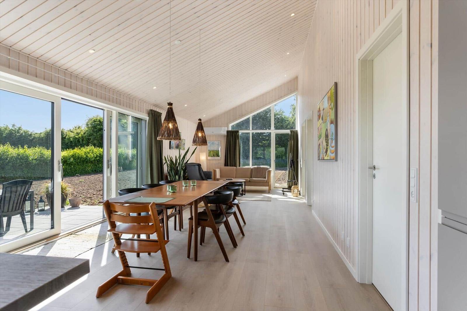Essbereich mit Tisch, Stühlen und Blick auf Garten. Wohnbereich mit Sofa und großen Fenstern.