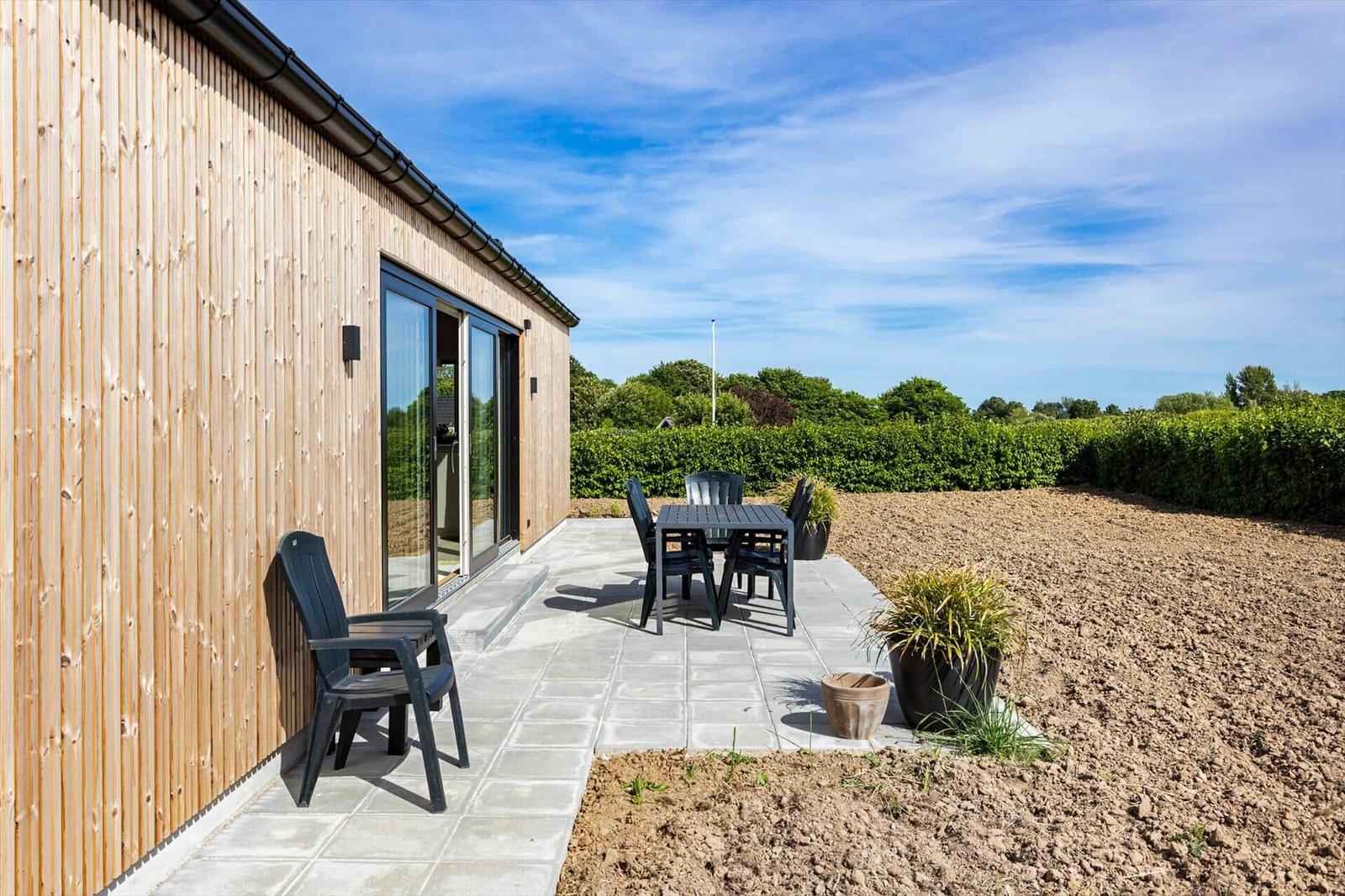 Terrasse mit Sitzgruppe neben Holzhaus. Hinterhof mit Beeten und Hecke.