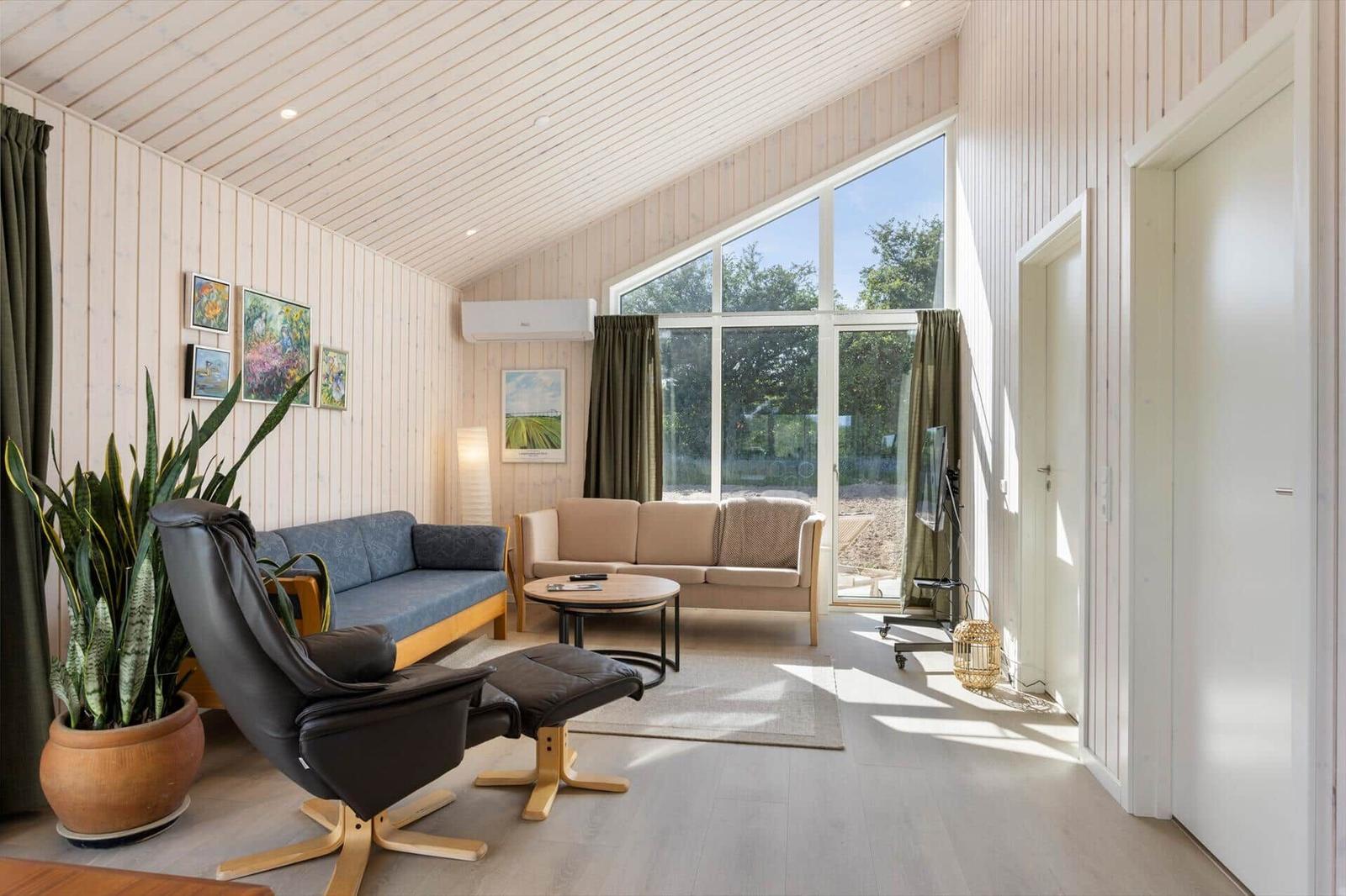 Wohnzimmer mit Sofa, Sessel und großen Fenstern. Holzwände und Boden.