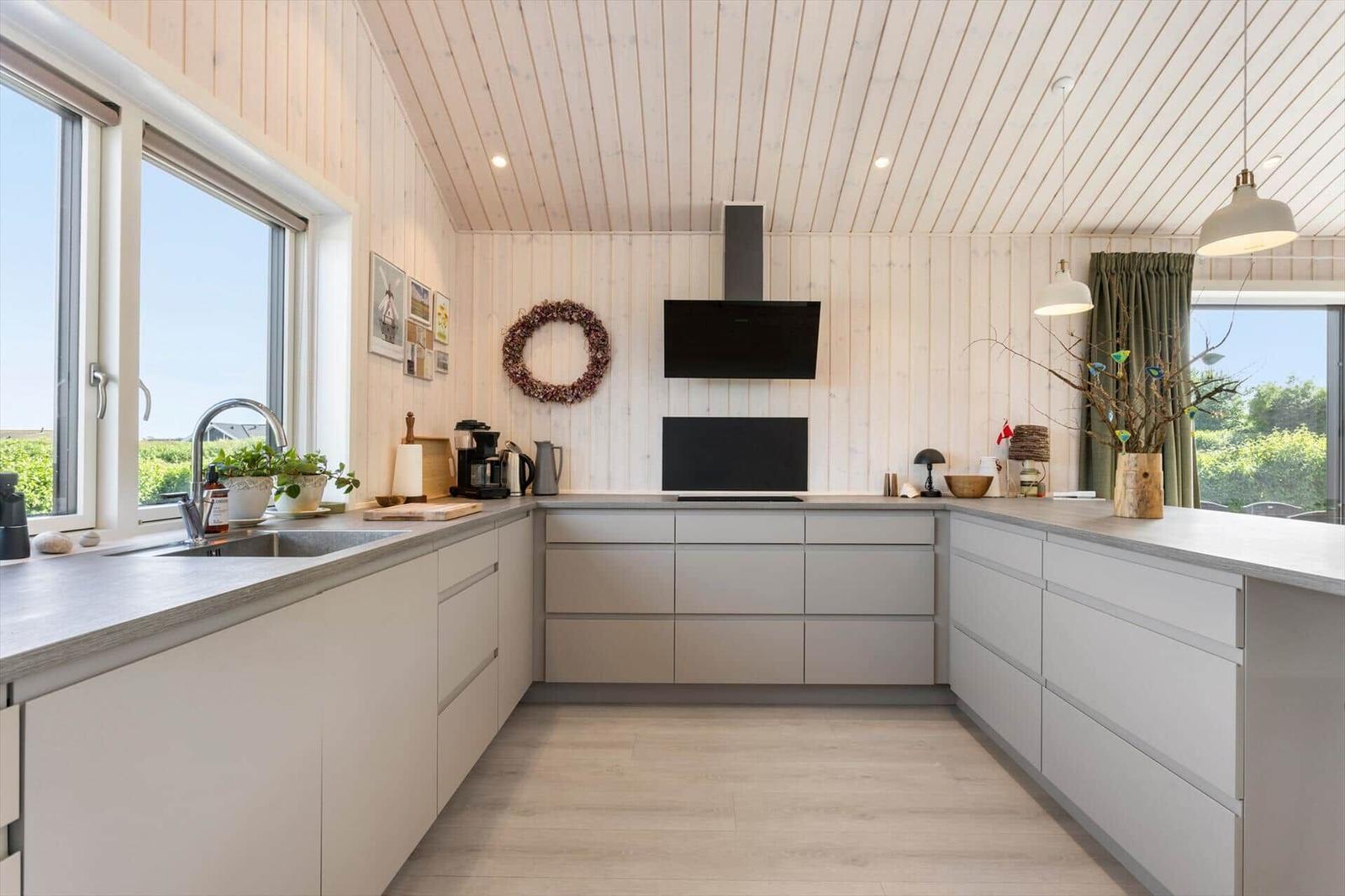 Moderne Küche mit Holzwand und Fenstern. Arbeitsplatte, Schränke und Küchengeräte sichtbar.
