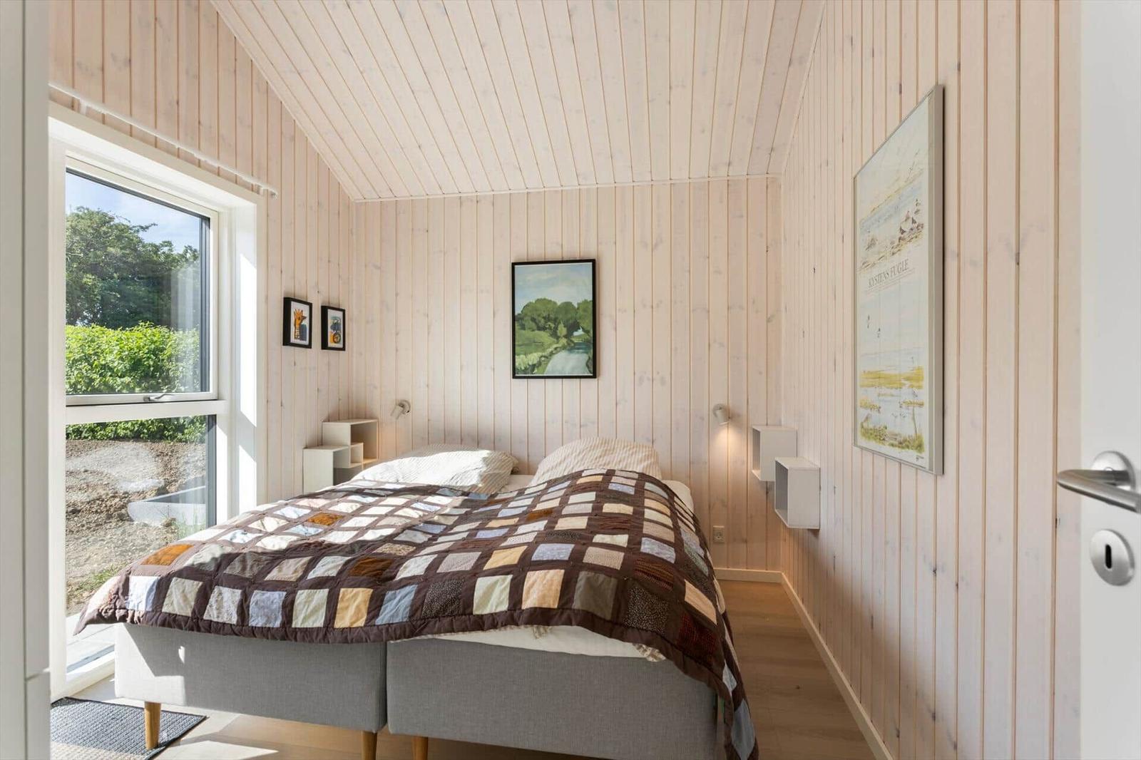 Schlafzimmer mit Holzwandverkleidung, Bett und Fenster zum Garten.