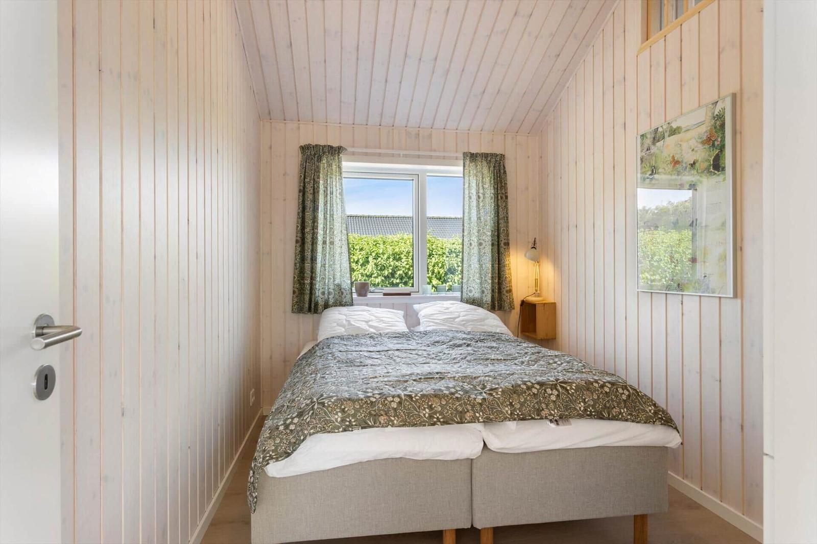 Schlafzimmer mit Bett, Fenster und Holzwandverkleidung.