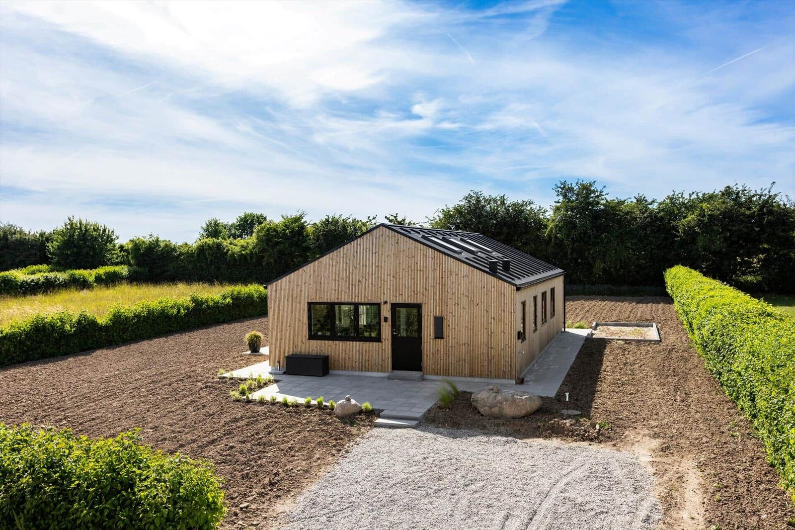 Moderne Holzhütte mit schwarzem Dach, umgeben von Feldern und Hecken.