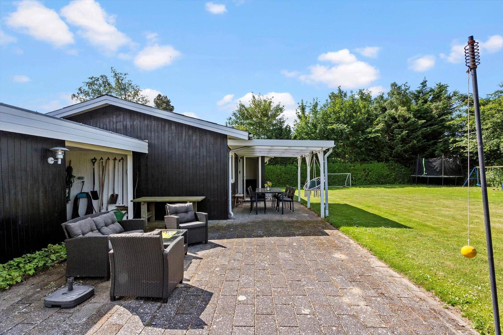 Hinterhof mit Terrasse, Gartenmöbeln und Spielplatz. Schwarze Hauswand und grüner Rasen.