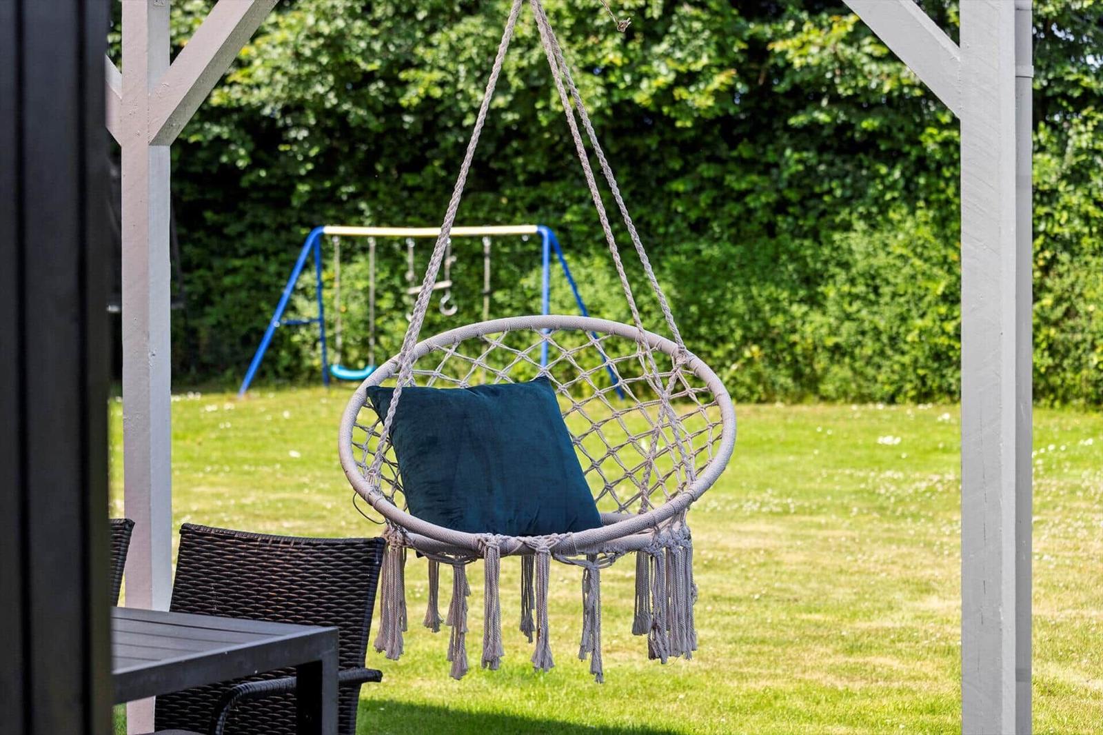 Hängesessel mit Kissen unter Pavillon im Garten mit Spielplatz im Hintergrund.
