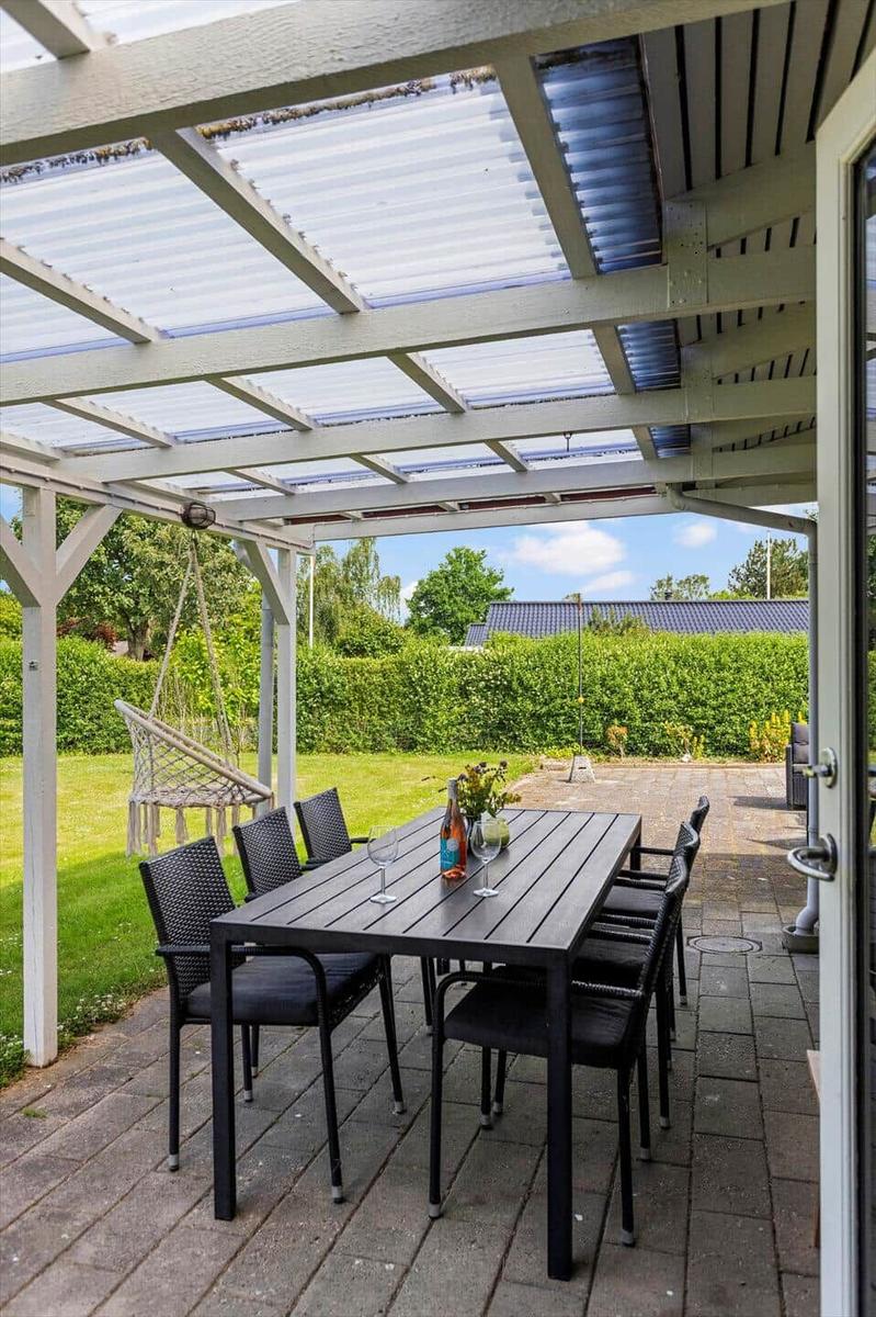 Gartenbereich mit Tisch, Stühlen und Schaukel unter einem Dach.