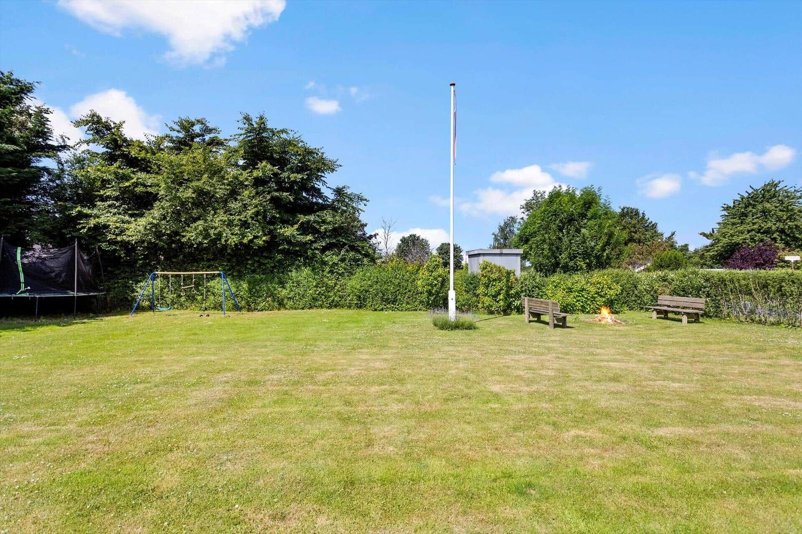 Großer Garten mit Spielplatz, Bänken und Feuerstelle unter blauem Himmel.