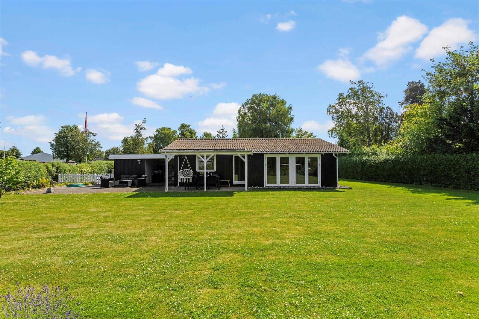 Ein Haus mit Terrasse, Garten und Hängesessel unter blauem Himmel.