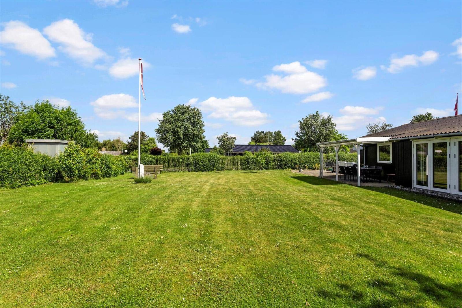 Großer grüner Garten mit Flagge, Terrasse und Sitzgelegenheiten neben dem Haus.