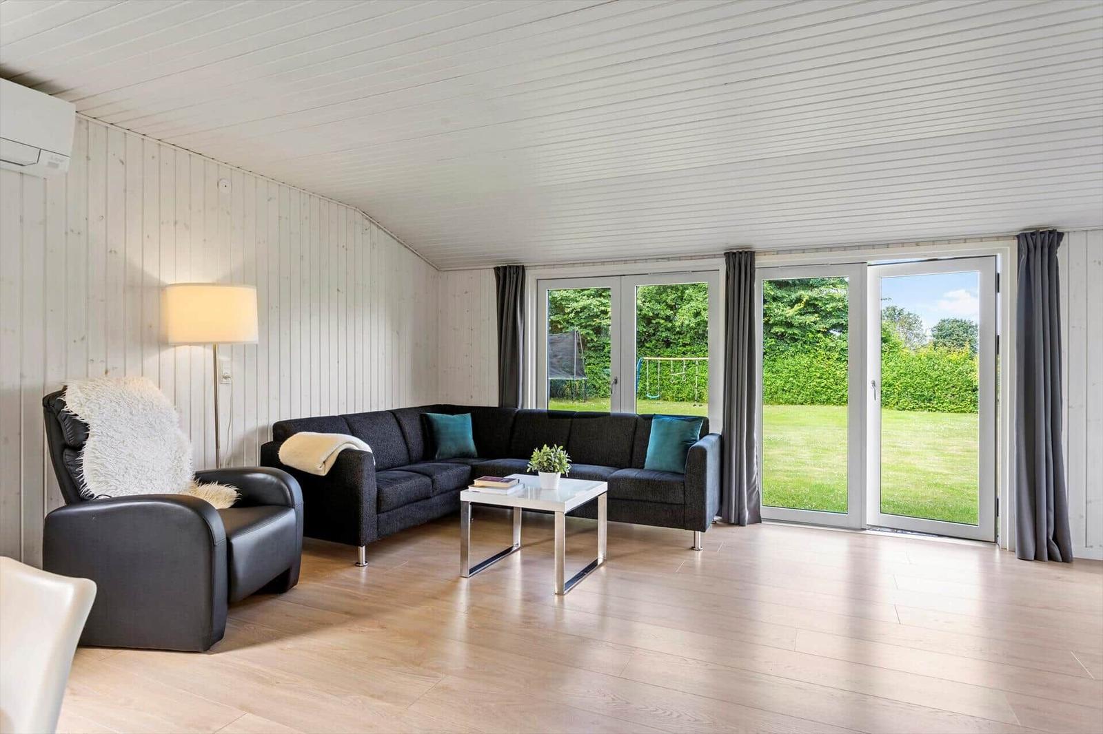 Wohnzimmer mit Sofa, Sessel und Glastür zur grünen Außenterrasse.