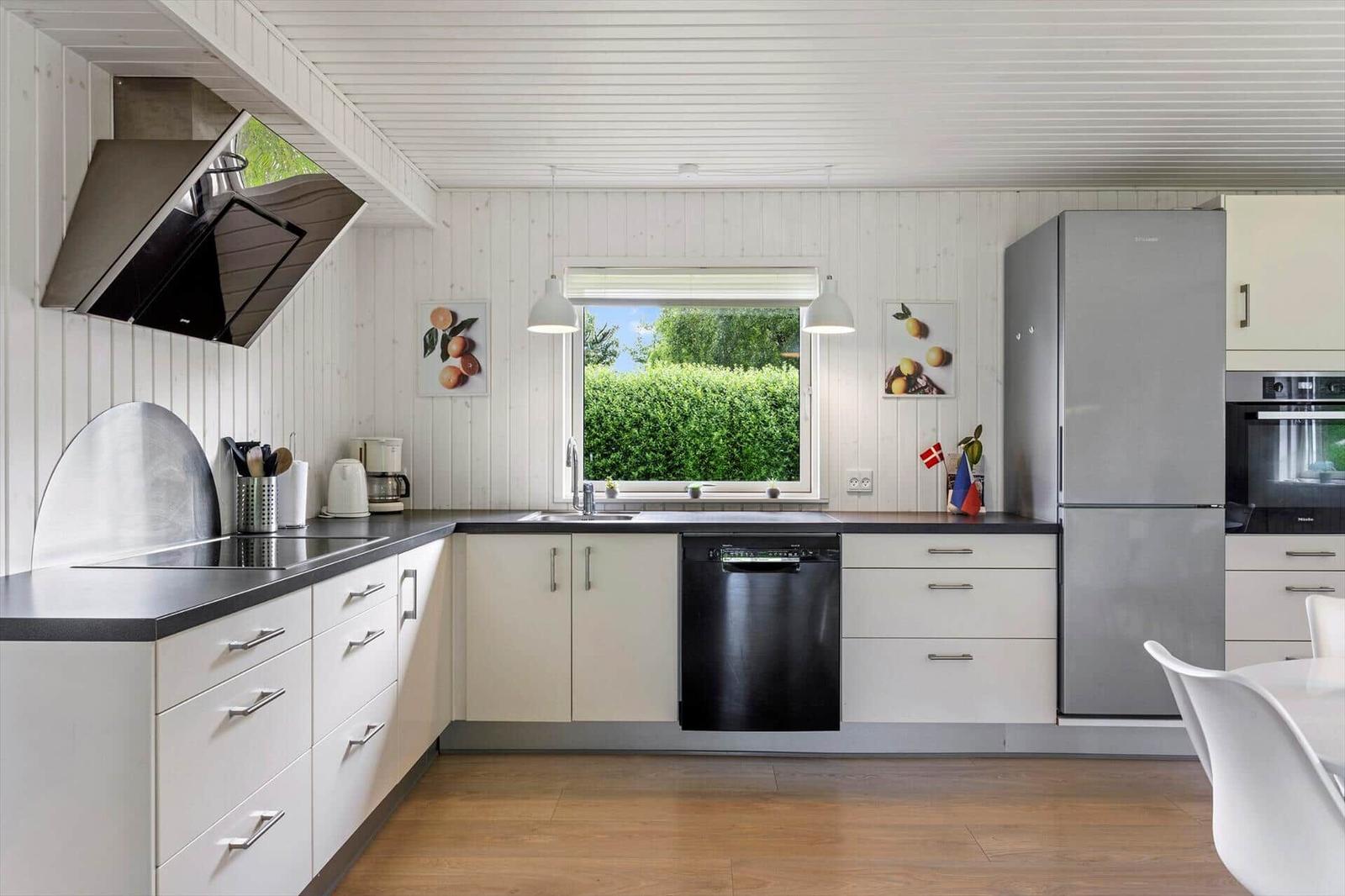 Moderne Küche mit weißer Arbeitsplatte, integriertem Spülmaschine und Blick auf grünen Hinterhof.