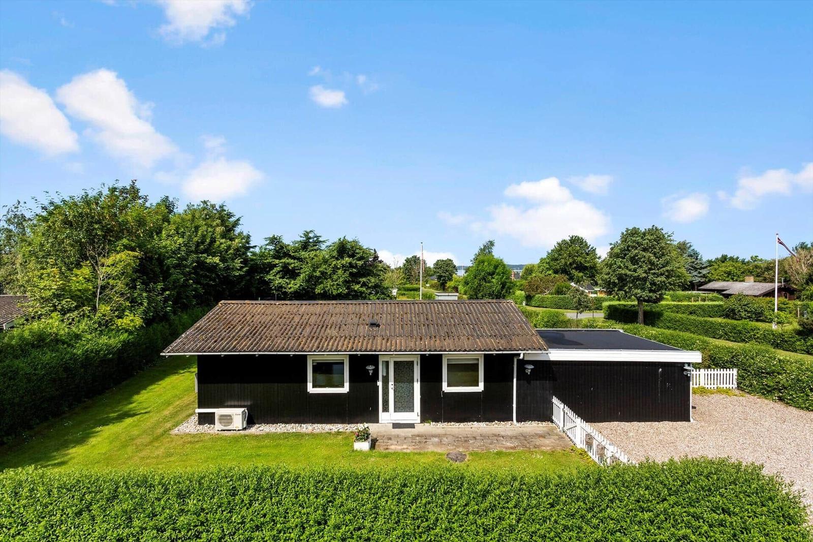 Schwarzes Haus mit weißen Fenstern und Tür, umgeben von Grün und einem Kiesweg.