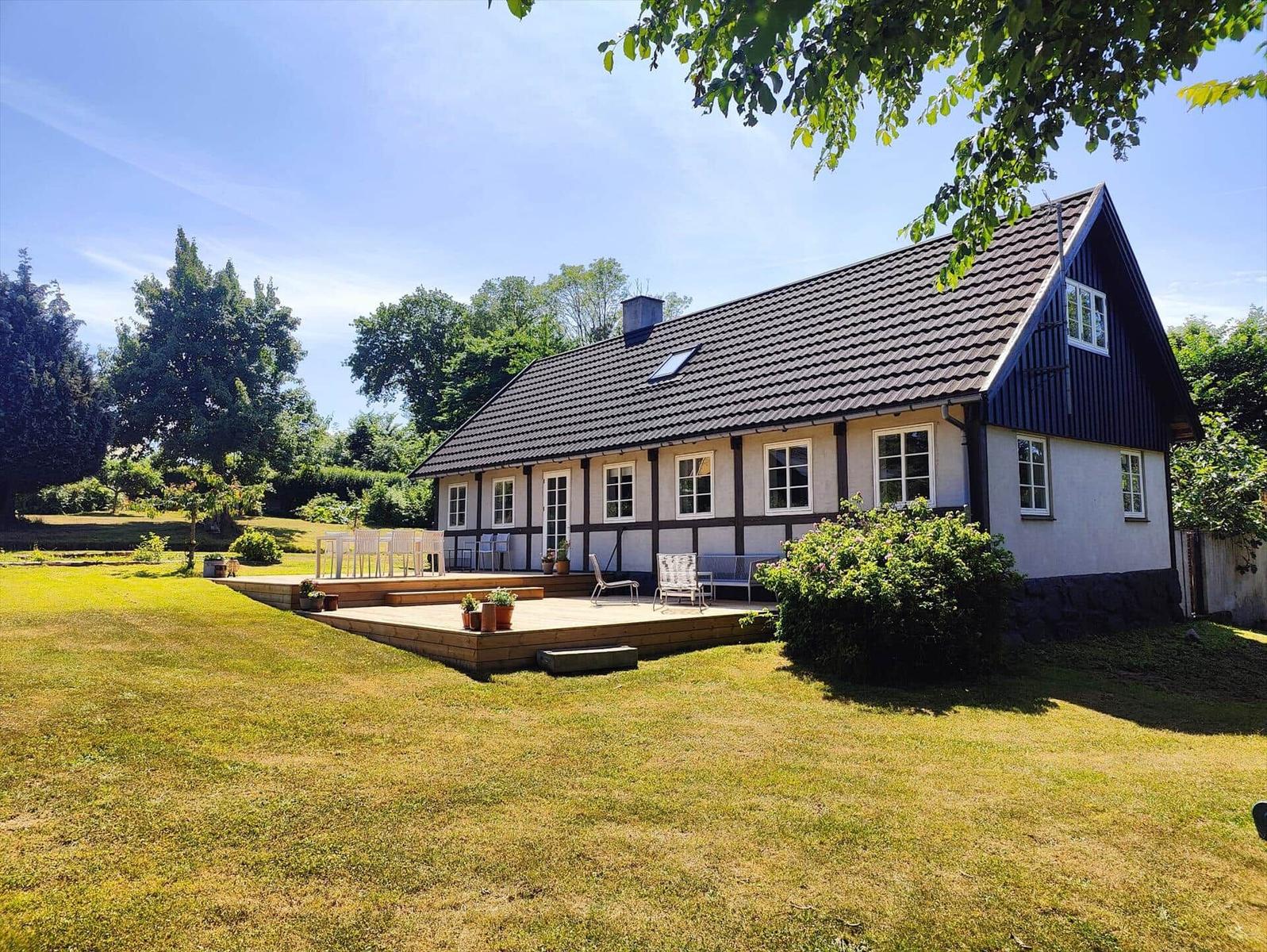 House with terrace, garden and trees under blue sky.