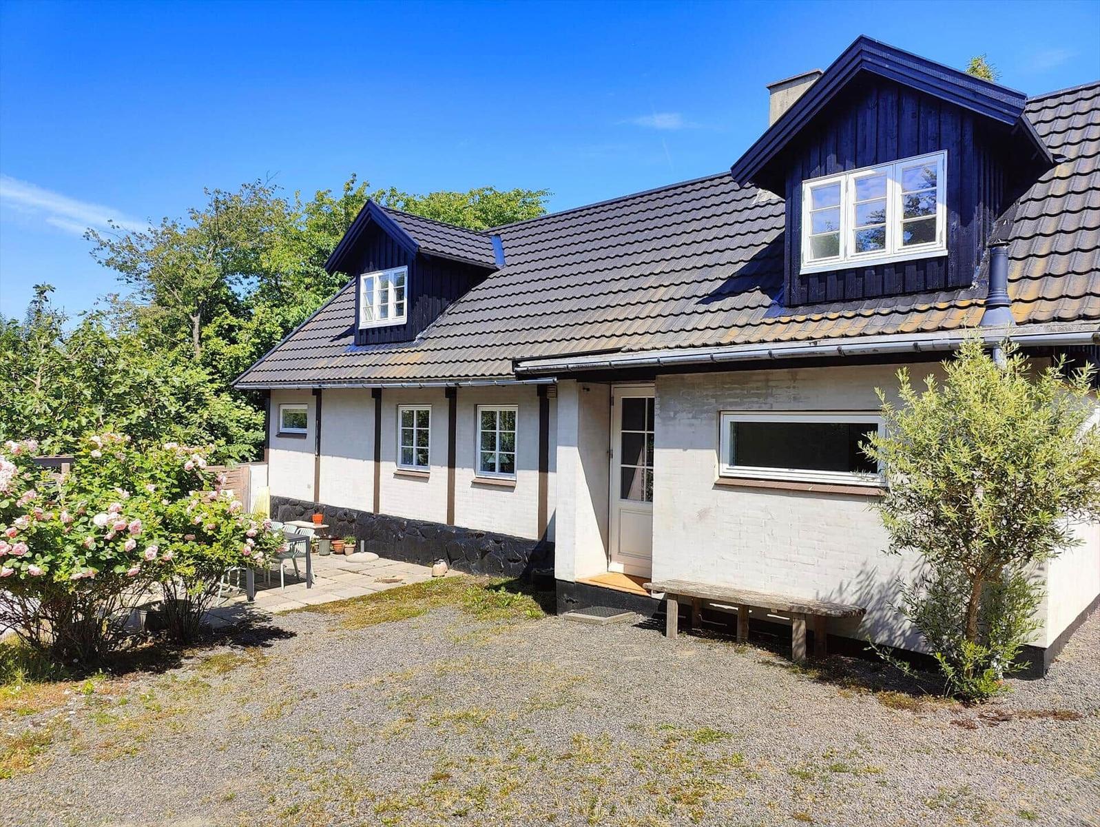 House with dark blue roof and white facade, surrounded by greenery and flowers.