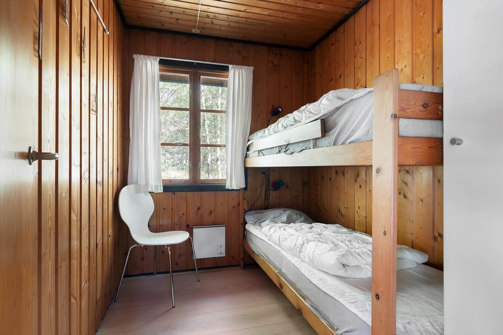 Ein Raum mit Holzwänden, einem Fenster, einer weißen Stuhl und einem Doppelstockbett.