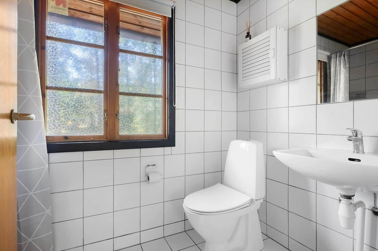 Badezimmer mit Toilette, Waschbecken und Fenster mit Blick auf die Natur.