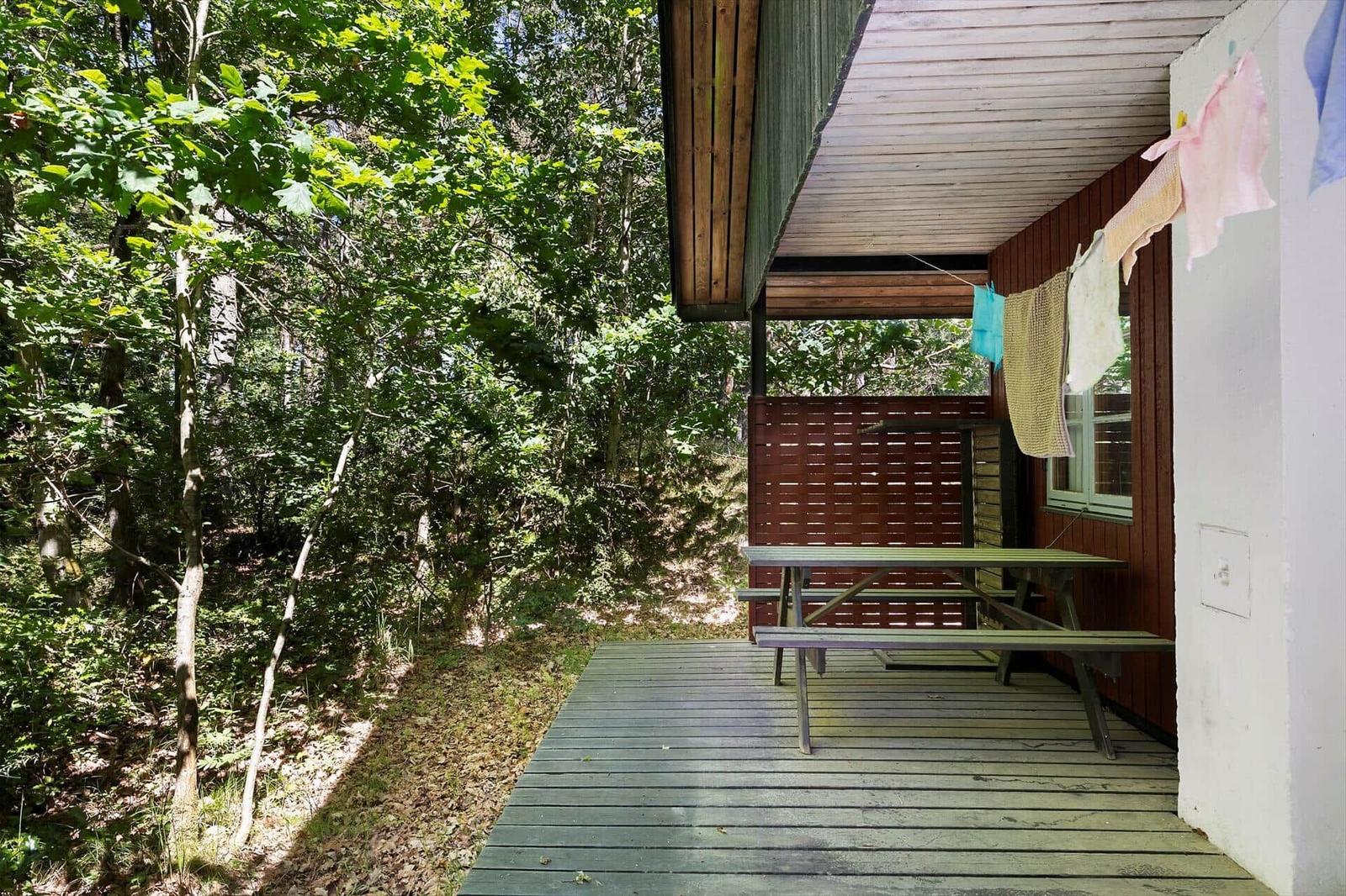 Terrasse mit Tisch und Bänken, Wäsche hängt zum Trocknen, umgeben von Wald.