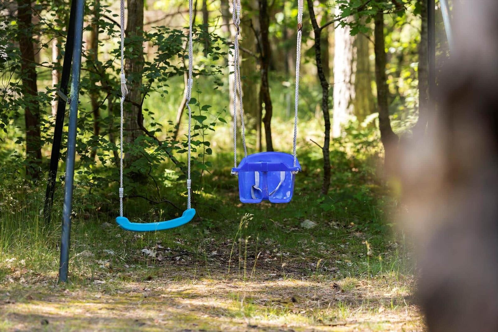 Zwei blaue Schaukeln hängen im Wald. Eine für Kinder, eine für Erwachsene.