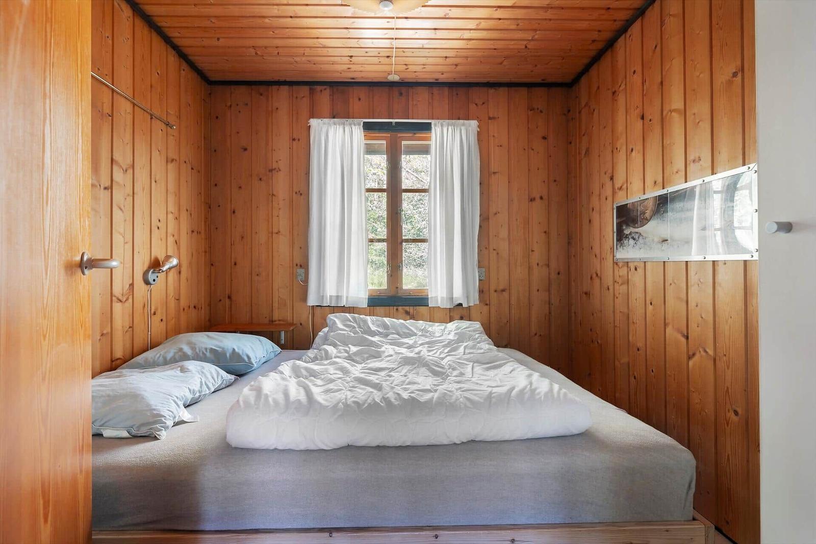 Schlafzimmer mit Holzwandverkleidung, Fenster und Bett.