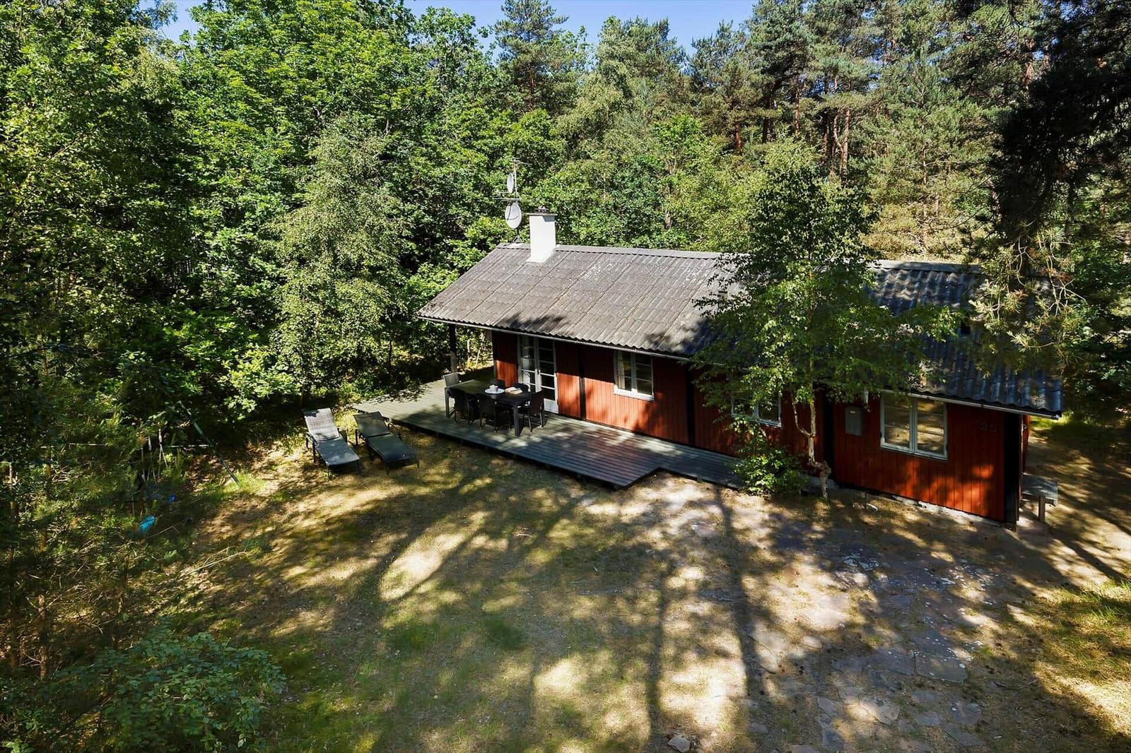 Roter Holzhaus mit Terrasse und Liegestühlen im Wald