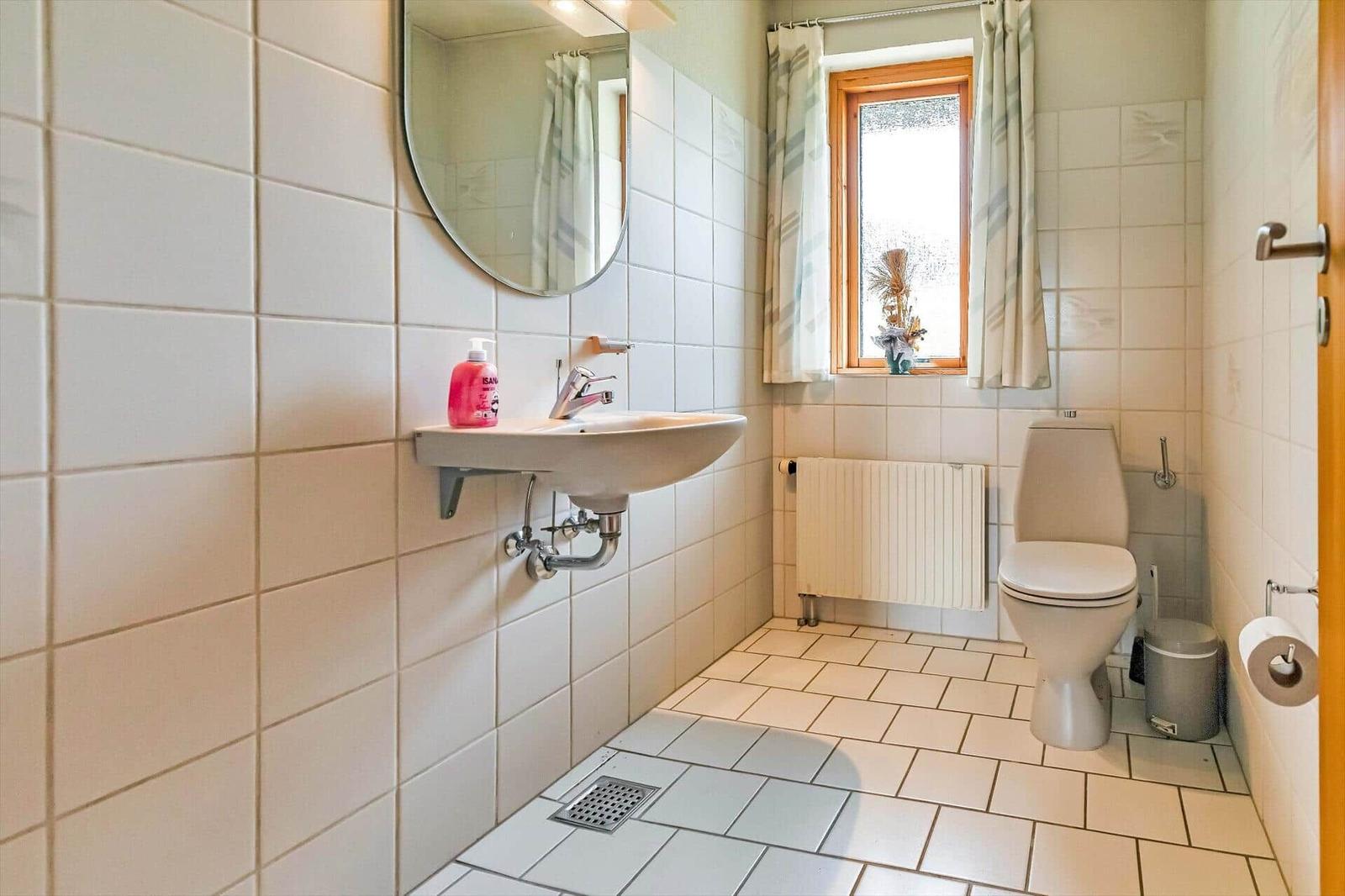 Bathroom with sink, toilet, and window with curtains.