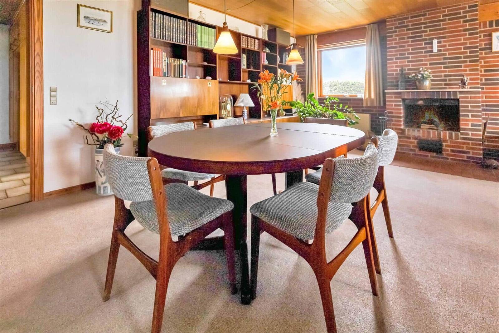 Round dining table with chairs, bookcase, and fireplace in living room.