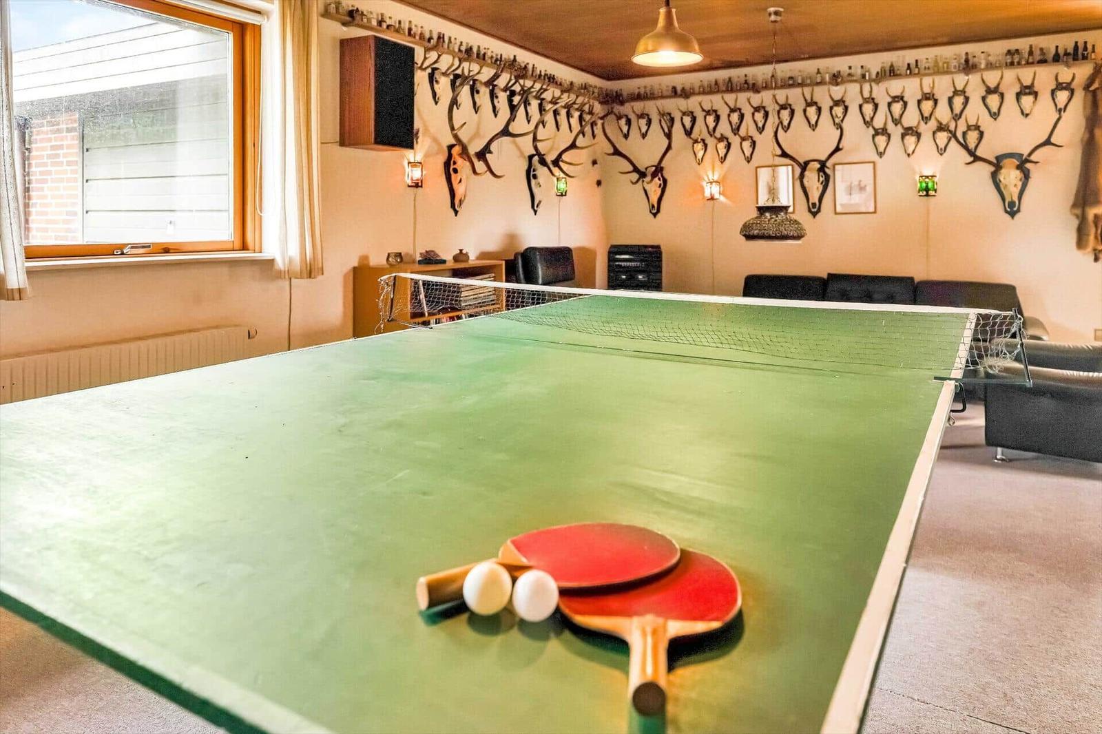 Ping pong table with paddles and balls. Wall with deer antlers and seating areas.