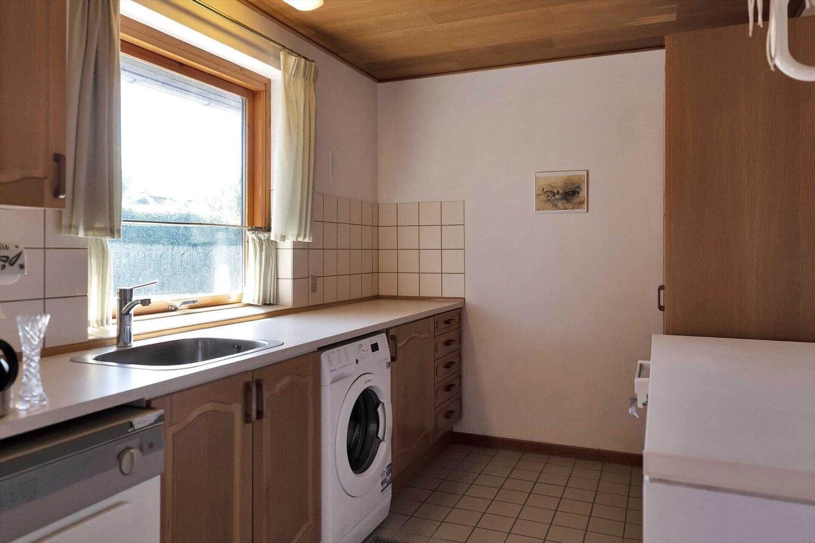 Kitchen with washing machine, sink, and window. Wooden surface and tiled floor.