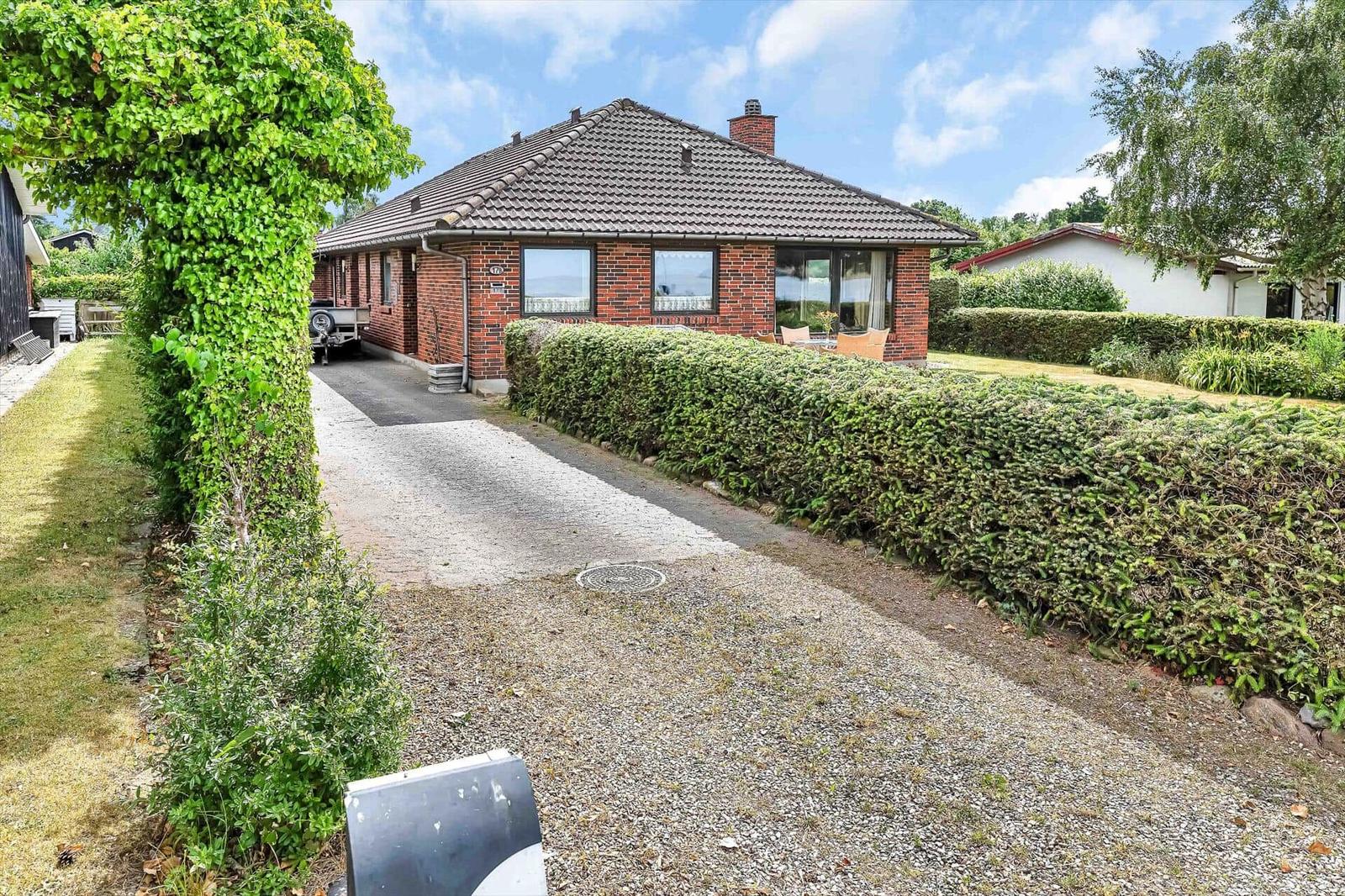 Drive to a house with red brick and green hedge fence.