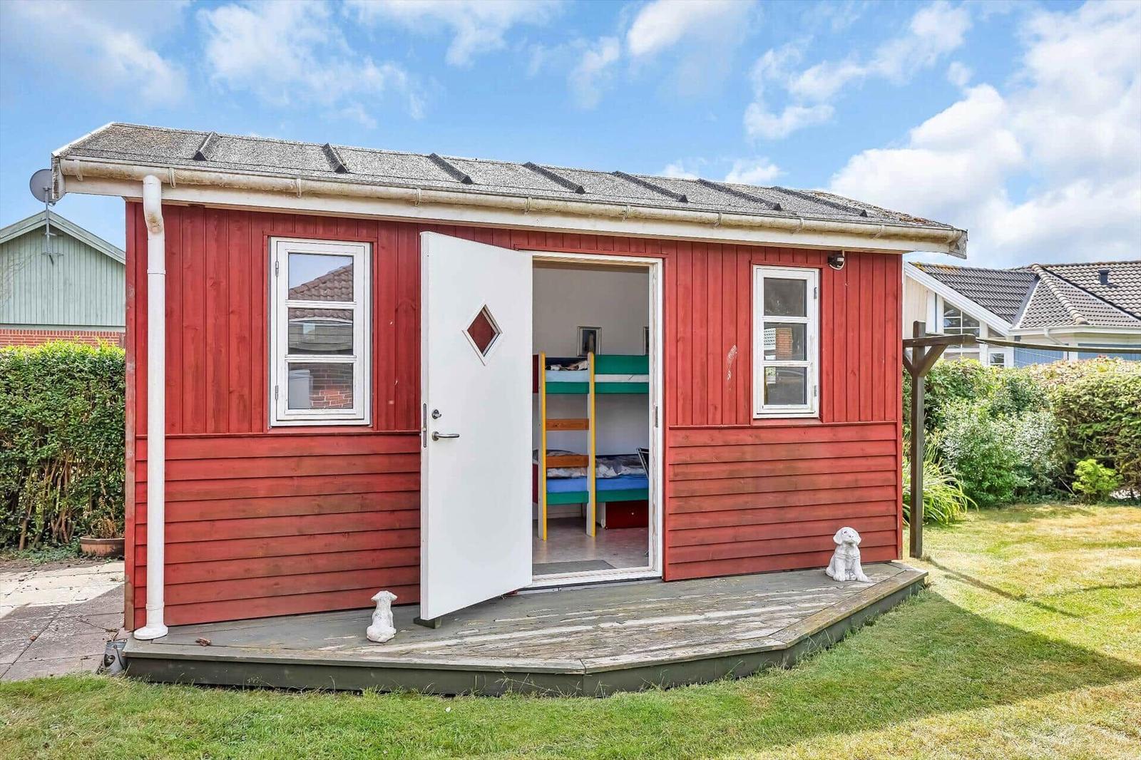 Red wooden house with open door, inside a bunk bed with green mattress.