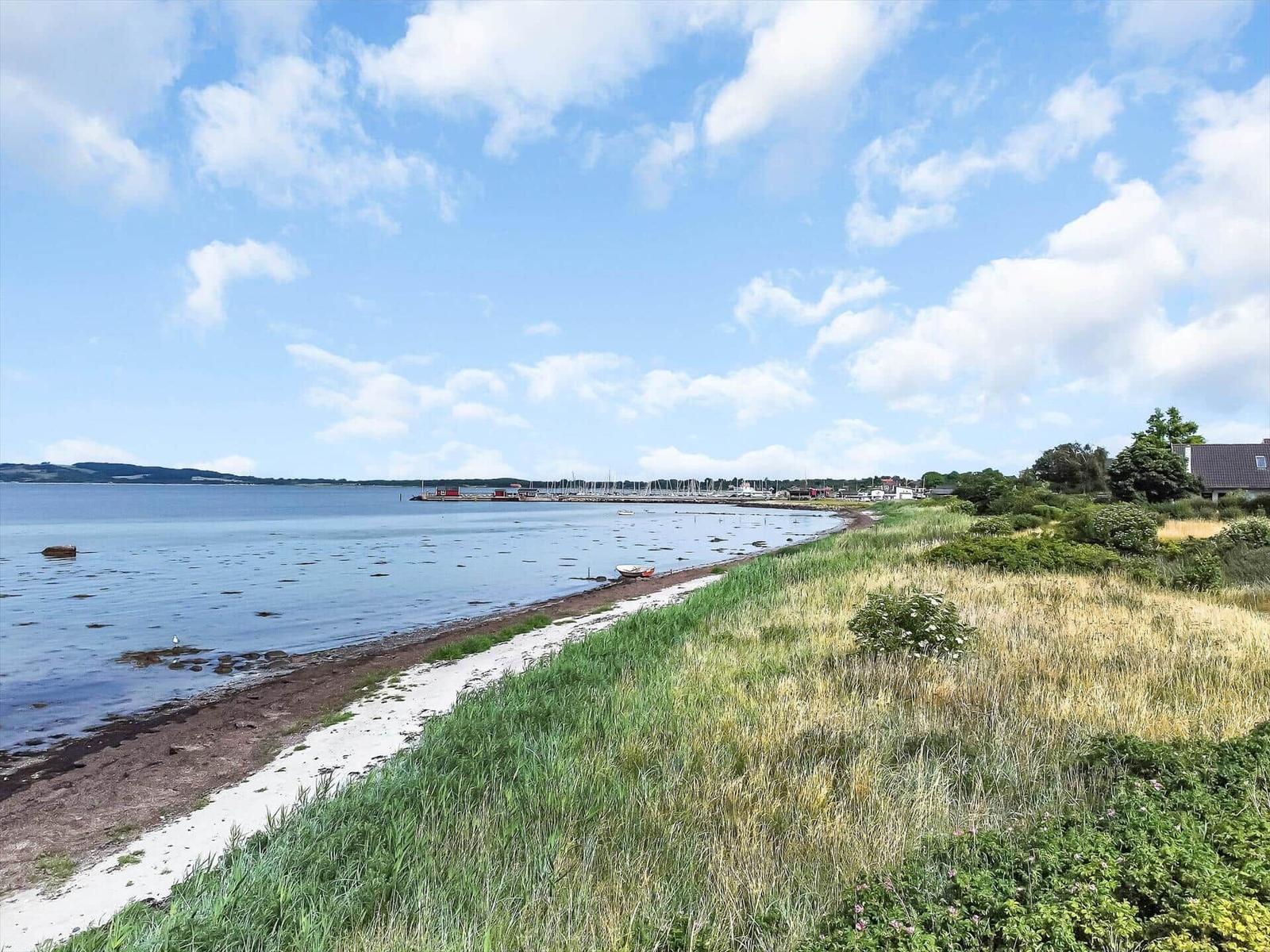 Seashore with grass, boats, and view of harbor and water.