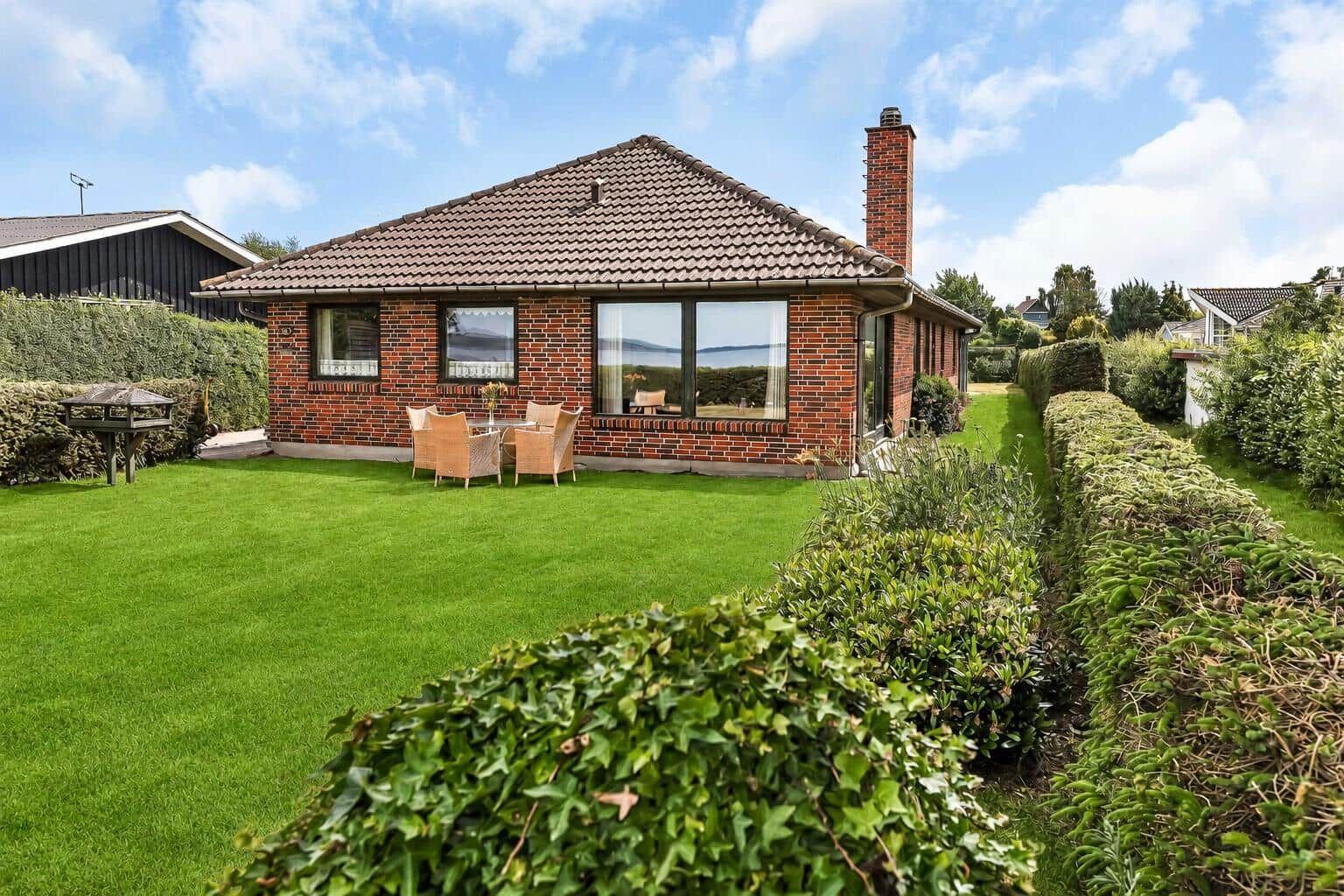 Red brick house with garden and seating. View of water and sky.