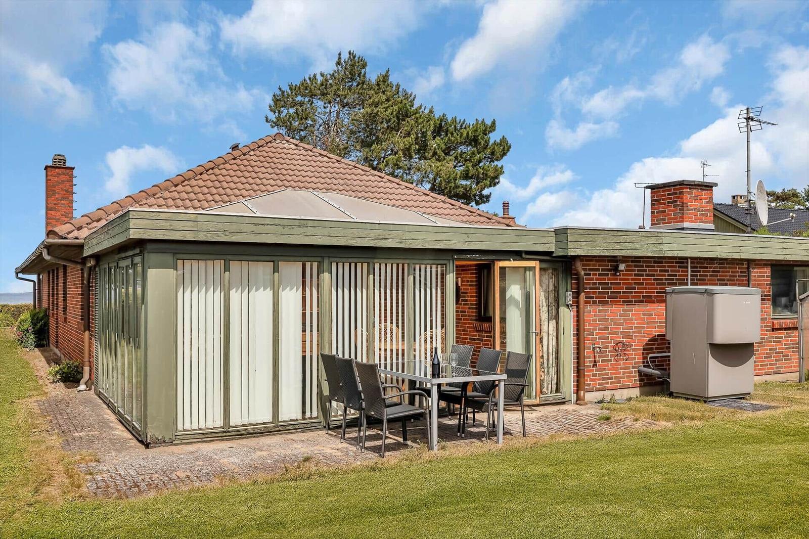House with terrace, garden, and barbecue area under blue sky.
