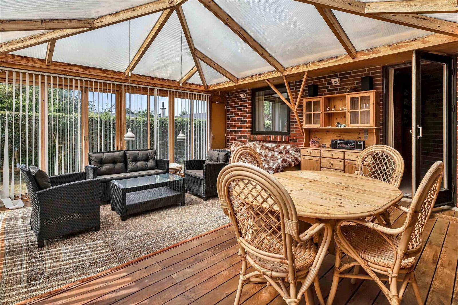 Terrace with seating area, dining table, and wooden deck. Glass roof and wooden frame visible.