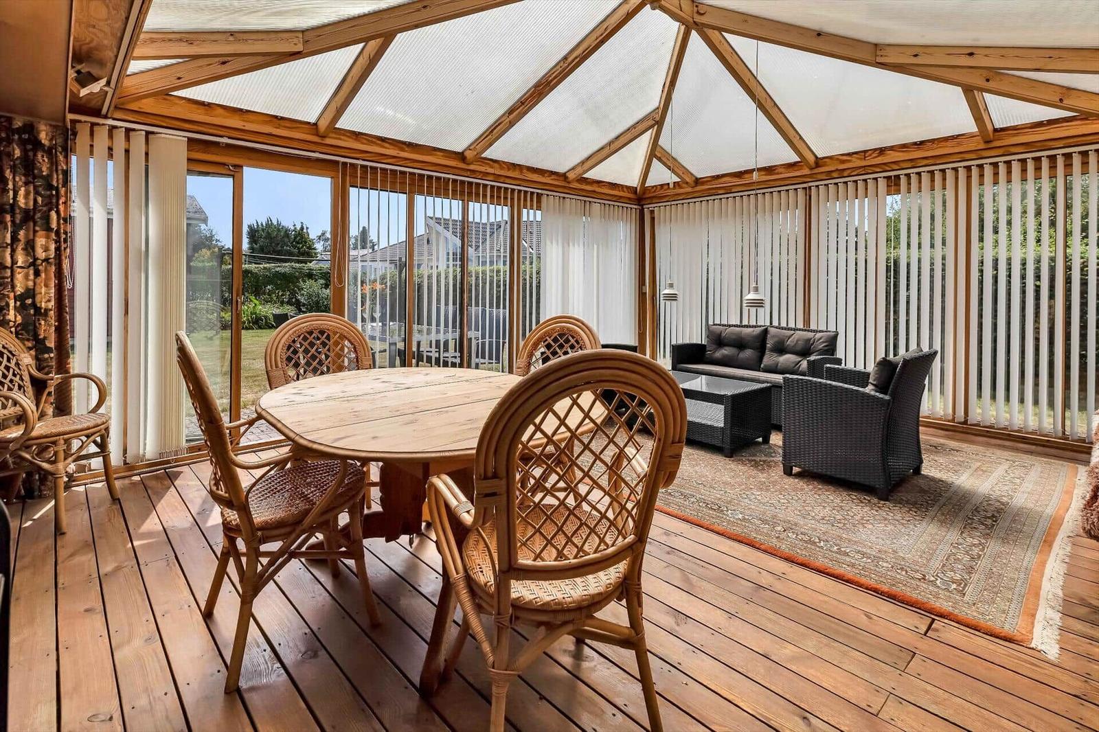 Terrasse mit Holzboden, runden Tisch und Stühlen, Sofa und Teppich.