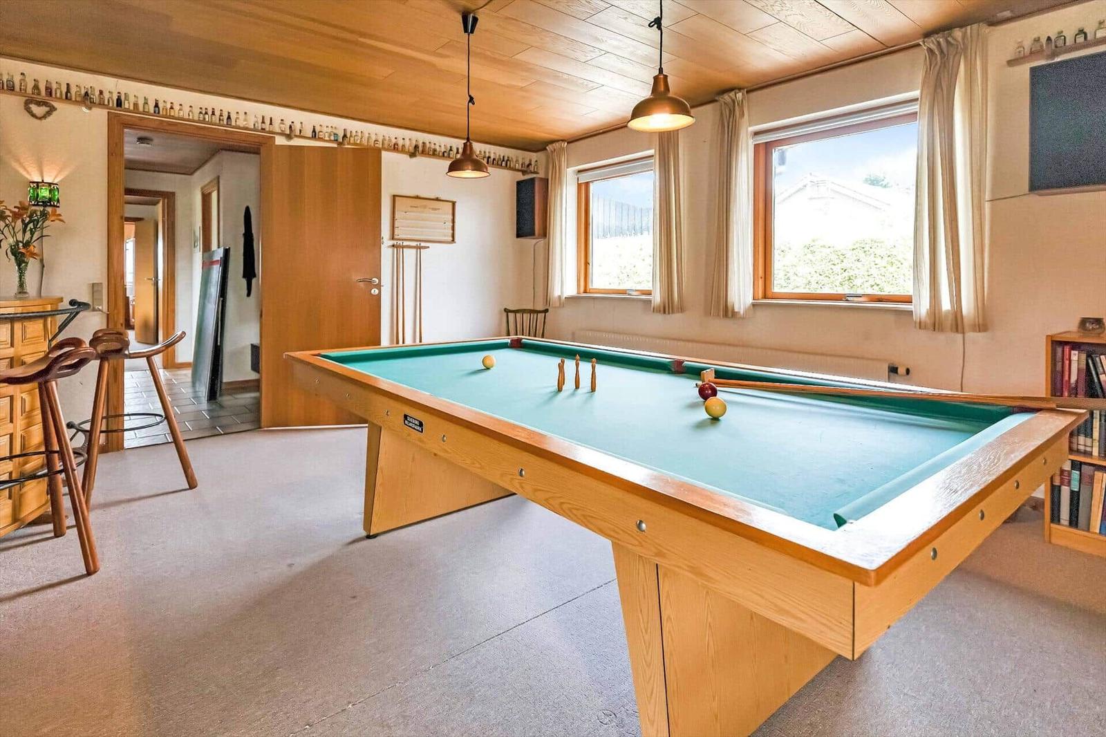 Pool table with green felt, windows, and bookshelf in room.