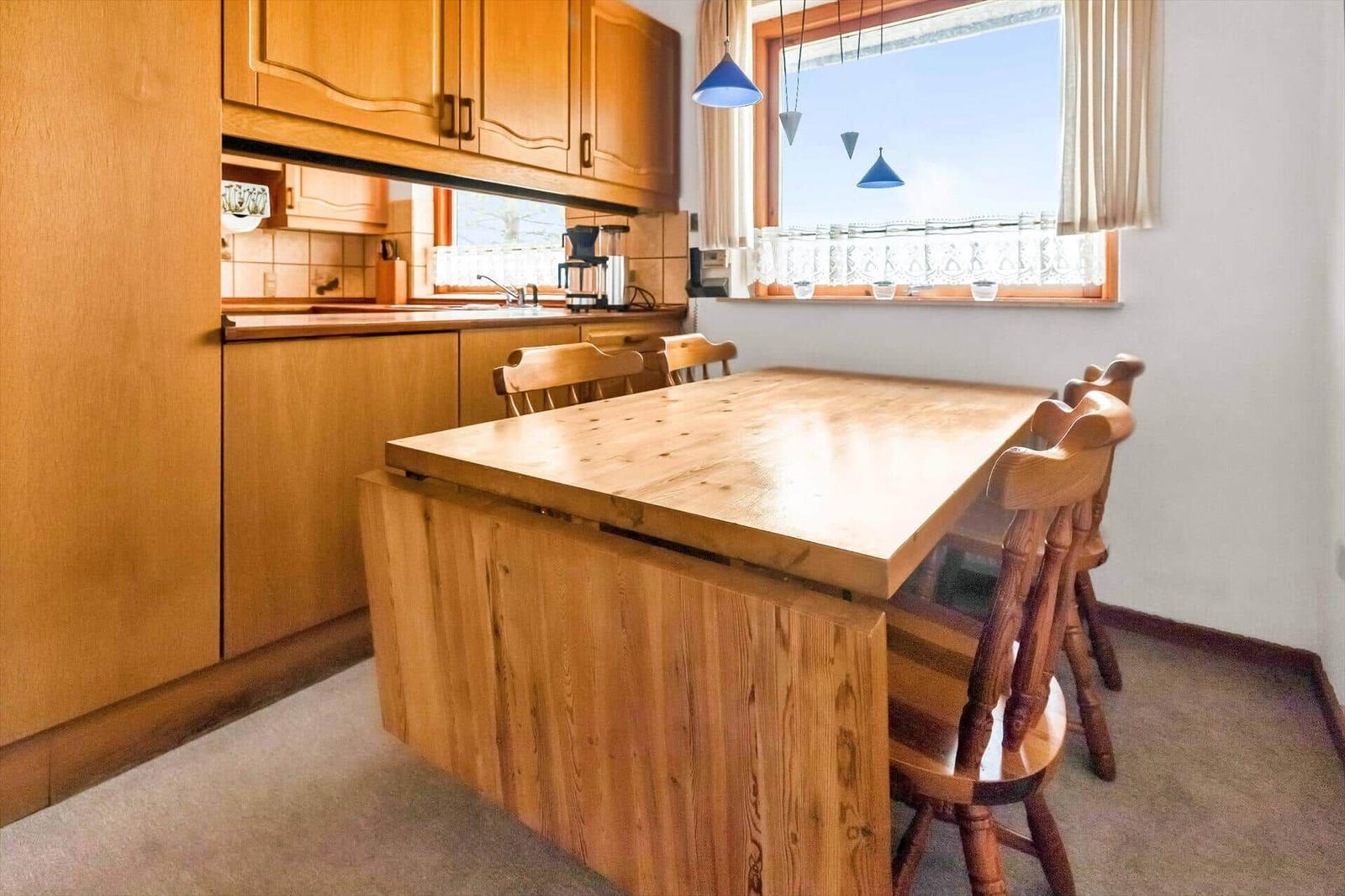 Kitchen with wooden table and chairs, window with curtain and pendant lamps.