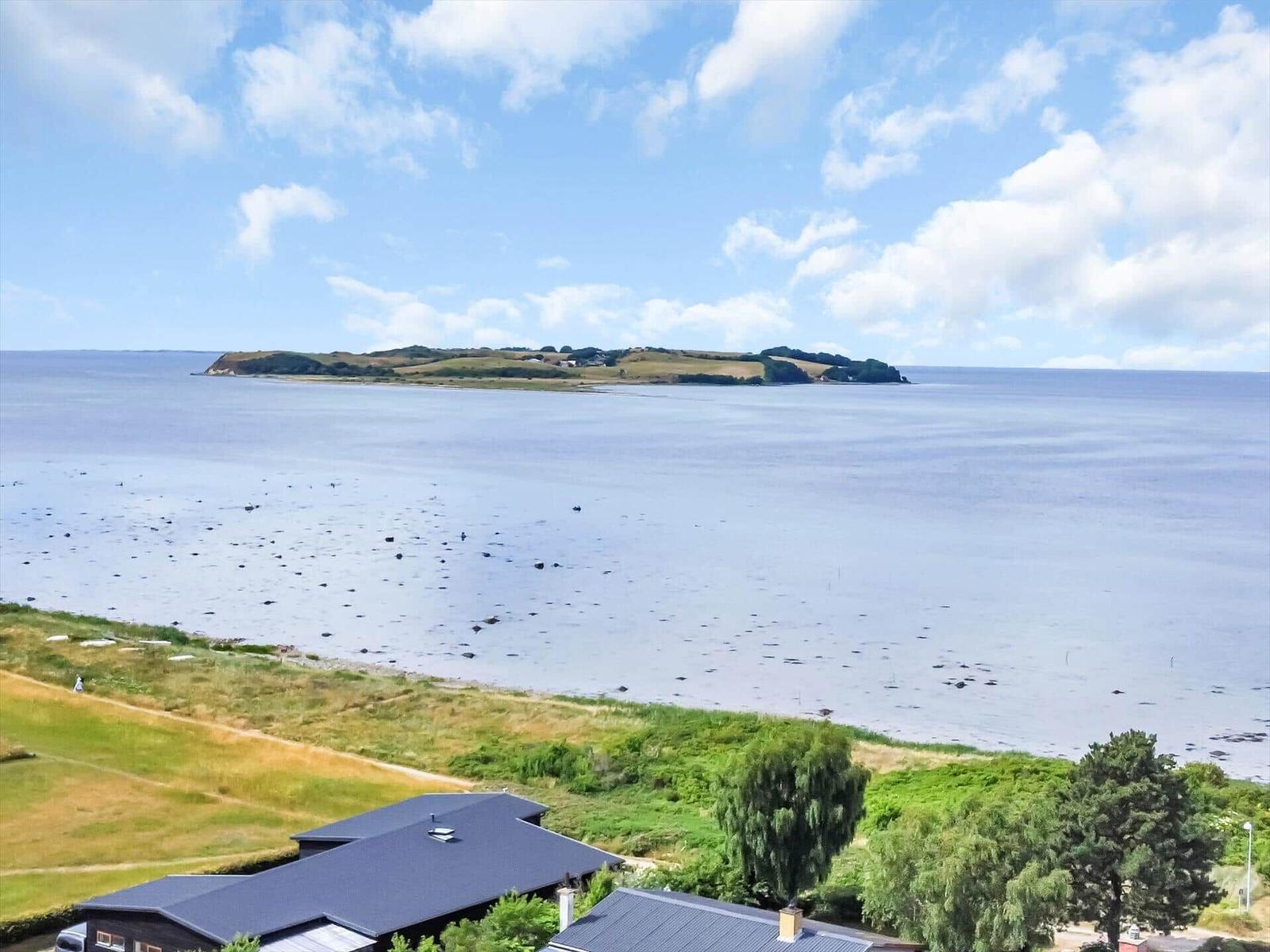 House with view of island and sea under blue sky with white clouds.