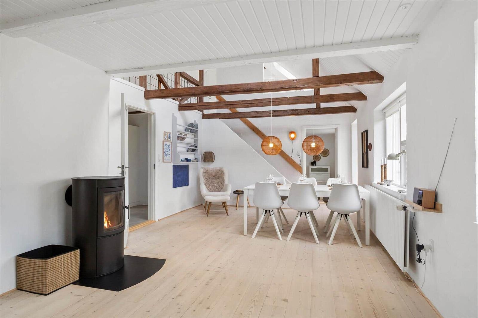 Raum mit Esstisch, Stühlen, Kamin und Holzbalken an der Decke.
