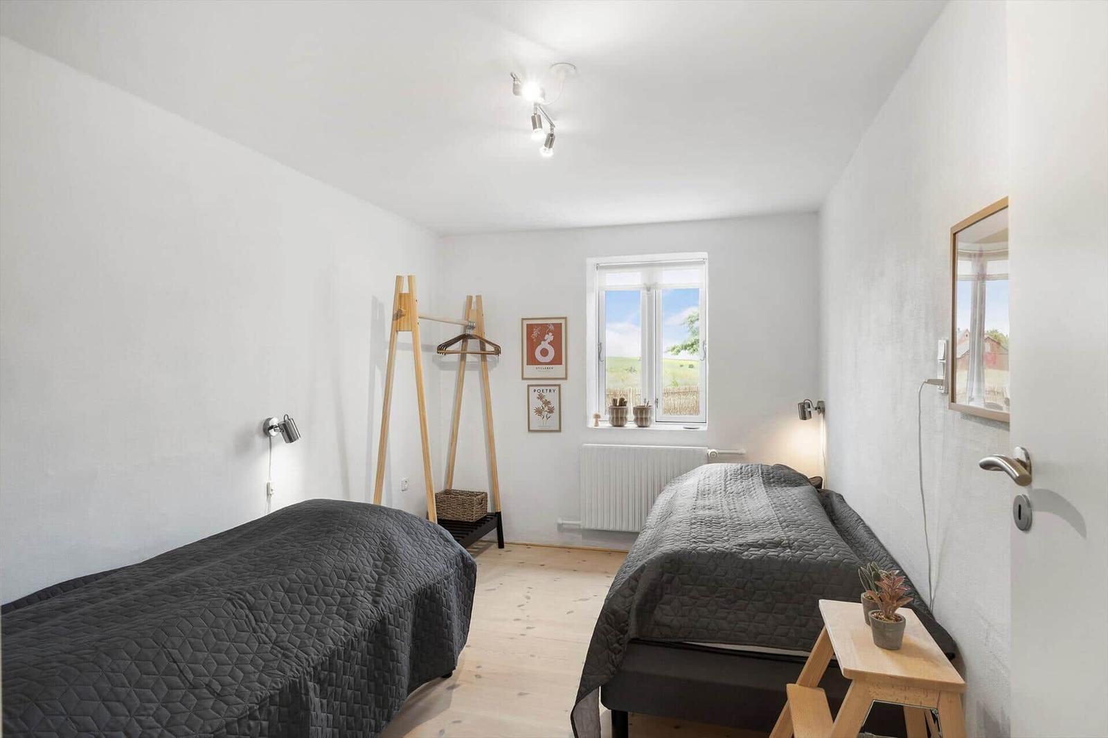 Zwei Betten, Kleiderständer, Fenster mit Blick auf Feld, Wandspiegel und Holztisch.