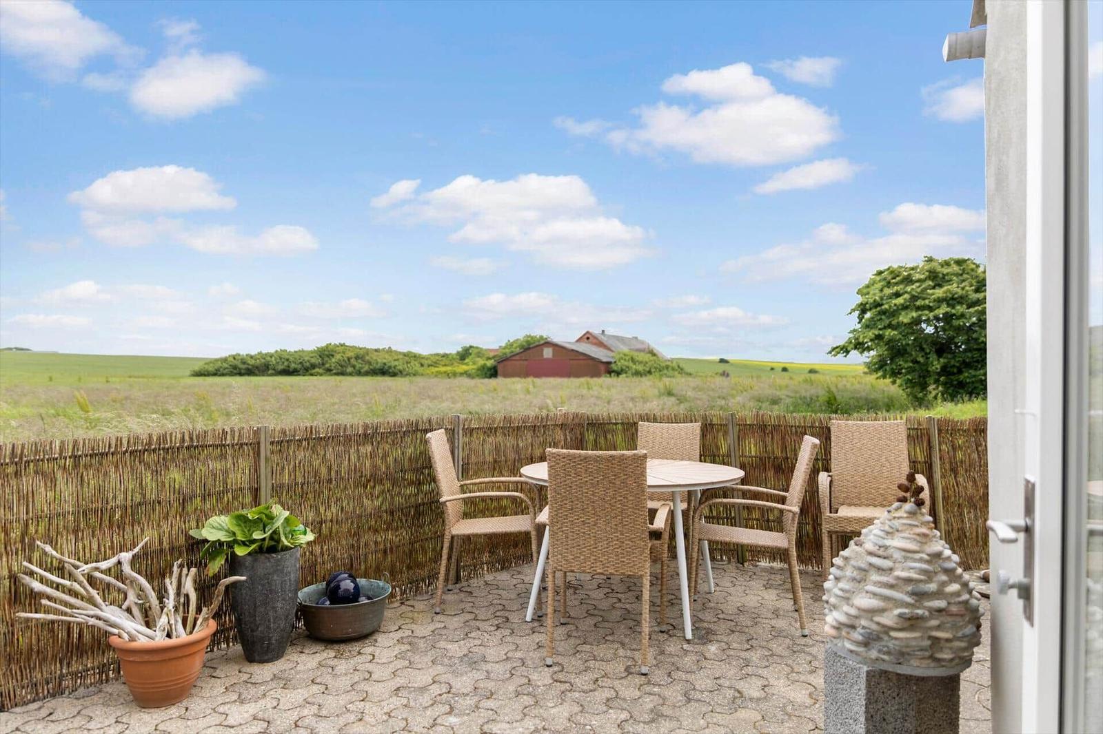 Terrasse mit Tisch und Stühlen, Blick auf Feld und rote Scheune unter blauem Himmel.