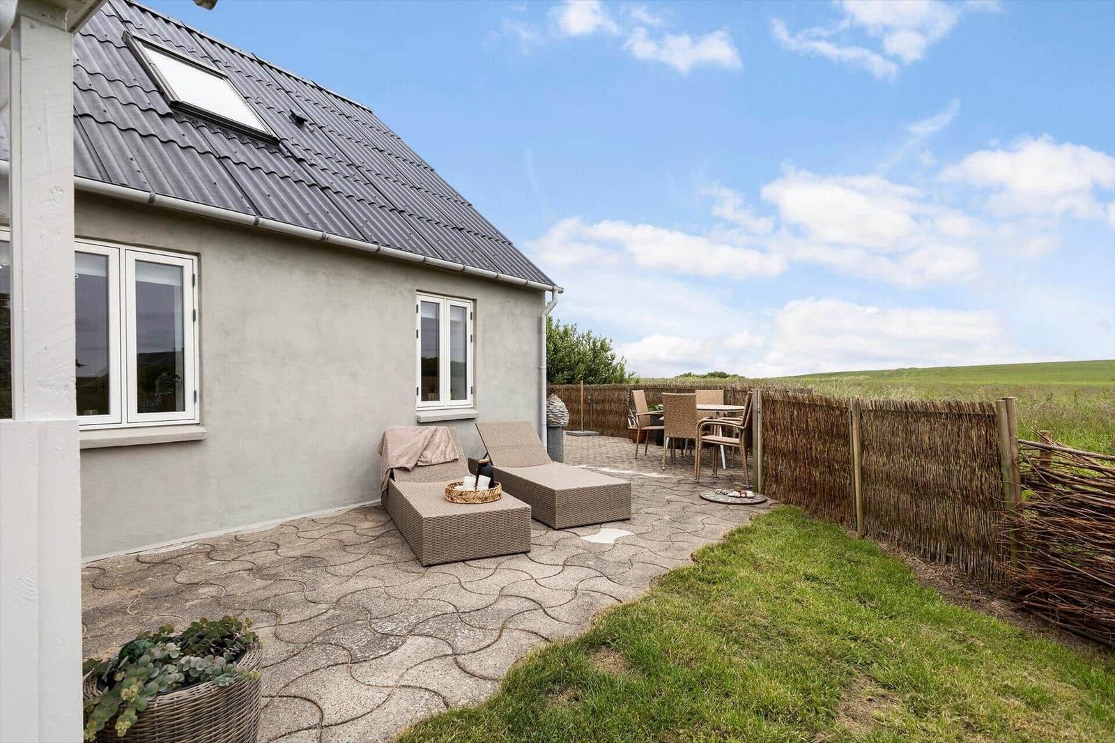 Terrasse mit Loungemöbeln und Sitzgruppe. Hinterhof mit Zaun und Grünfläche.
