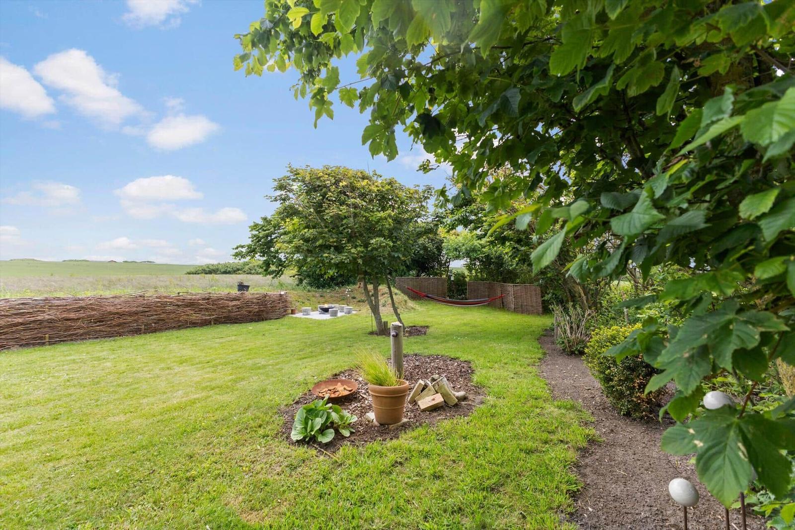 Grüner Garten mit Baum, Hängematten und Blick auf Felder.