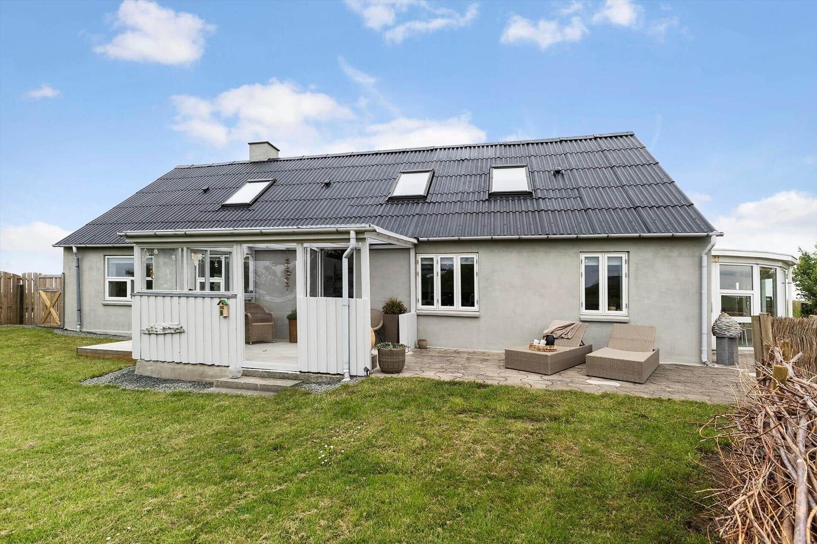Ein Haus mit grauer Fassade, Dachgauben und einer Terrasse mit Gartenmöbeln.